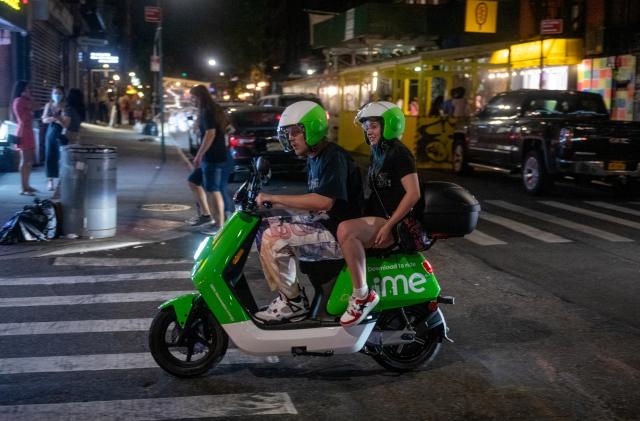 NEW YORK, NEW YORK - MAY 22: People without masks drive around on a Lime E-moped in the Lower East Side on May 22, 2021 in New York City. This is the first Saturday night that New York City is not under pandemic restrictions in more than a year. On May 19, all pandemic restrictions, including mask mandates, social distancing guidelines, venue capacities and restaurant curfews were lifted by New York Governor Andrew Cuomo. (Photo by Alexi Rosenfeld/Getty Images)