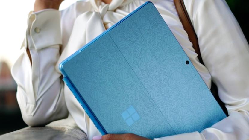 Lifestyle image of the Microsoft Surface Pro 9. A person holds a blue (patterned) version of the hybrid device (back-facing).