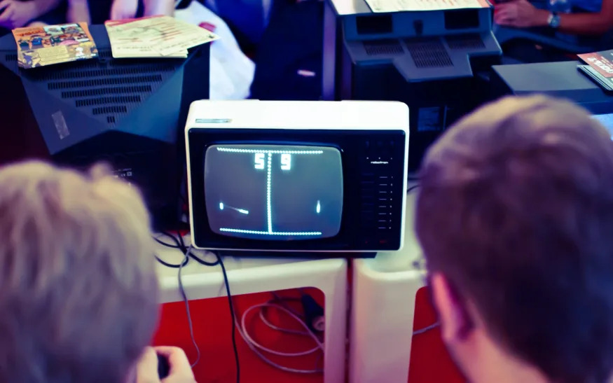 Two individuals playing Pong on an old CRT TV. The score is 9 to 5. 
