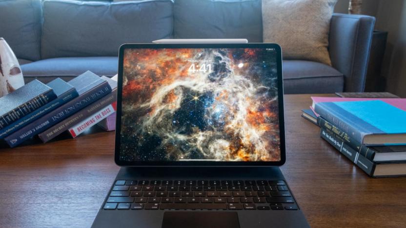 An iPad Pro with a dynamic galaxy wallpaper sitting on a desk with books. A couch looms behind it.