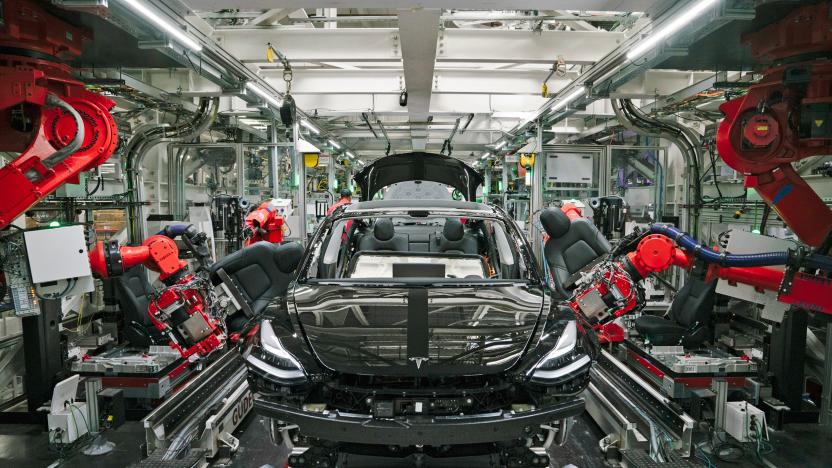 A photograph of the front of a Tesla car while it's being assembled by robots on the assembly line.