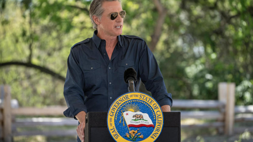 A man wearing a blue dress shirt and sunglasses standing behind a podium 