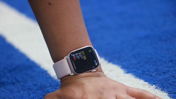 Closeup of a person’s left hand on a track's starting line. They wear the Apple Watch Series 9 on their wrist with a tracked workout on its screen.