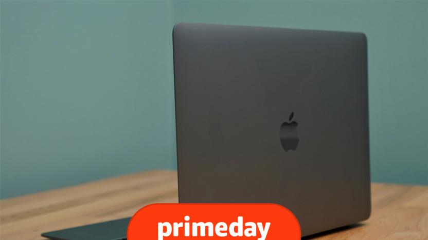 A silver MacBook Air laptop sits on a brown desk in front of a blue wall, with its back facing the camera at an angle, showcasing an Apple logo.