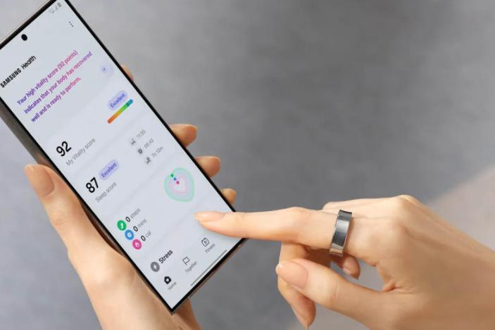 Galaxy Ring lifestyle image, showing a person wearing the ring on their left index finger while navigating the Samsung Health app on a Galaxy smartphone.