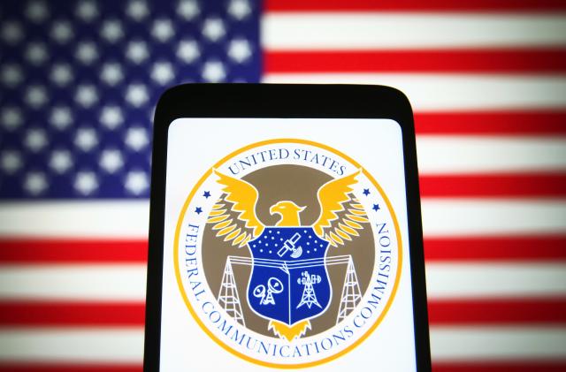 UKRAINE - 2021/11/25: In this photo illustration, U.S. Federal Communications Commission (FCC) seal is seen on a smartphone screen with the US flag in the background. (Photo Illustration by Pavlo Gonchar/SOPA Images/LightRocket via Getty Images)