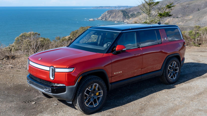 Photo of the Rivian R1S electric SUV (red) sitting by a beach with rocky shores.