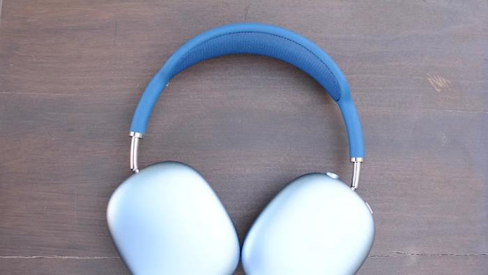 The blue Apple AirPods Max headphones lay flat on a brown wooden tabletop.