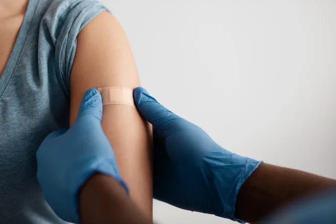 Vaccination of patients in hospital against covid-19 pandemic. Hands of african american doctor in protective gloves puts band aid to inculcate site to patient in clinic, close up, free space, cropped