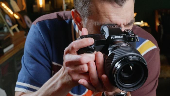 A man holding the Fujifilm GFX100S II up to his eye, with the lens pointing out.