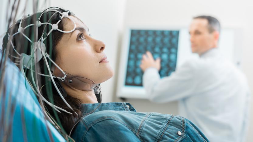 Vital procedure. Beautiful dark-haired woman lying on an examination table and undergoing electroencephalography while her doctor examining CT results