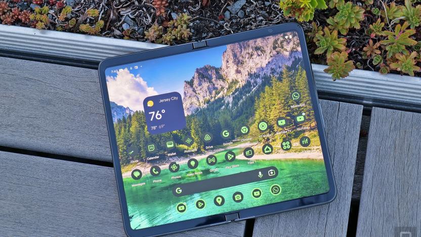 The Google Pixel Fold seen from above in its wide-open tablet-like form as it rests on a bench connected to a planter (small plants are seen in the edge of the shot).