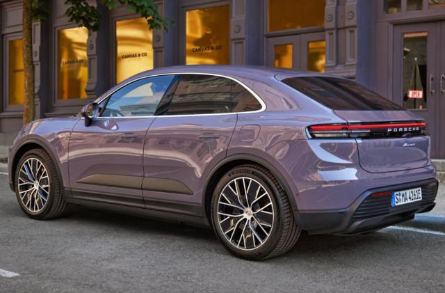 A purplish-grey Porsche’s all-electric Macan SUV is parked on the side of a road in front of doorways and windows.