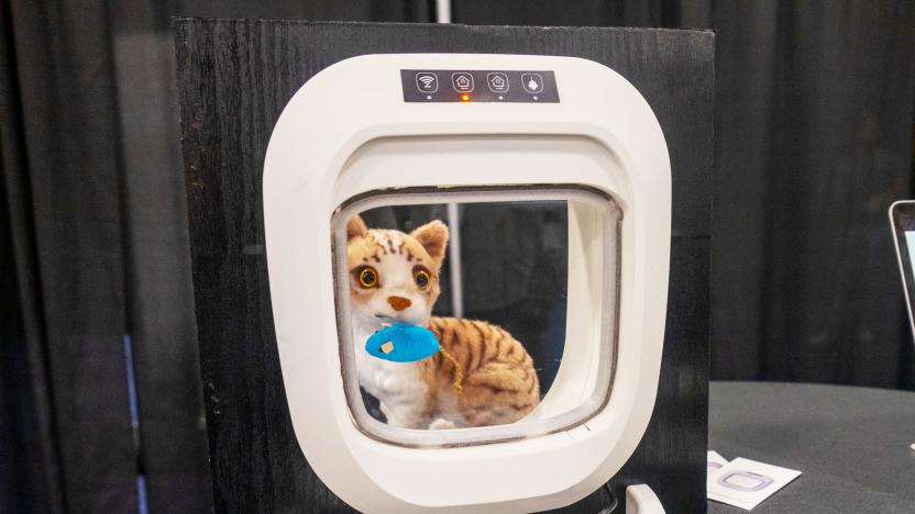 A white Flappie cat door installed in a square of black wood with a stuffed cat and mouse behind it on display at CES 2024.