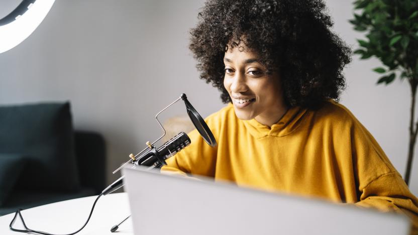 Young woman podcasting while looking at laptop at home