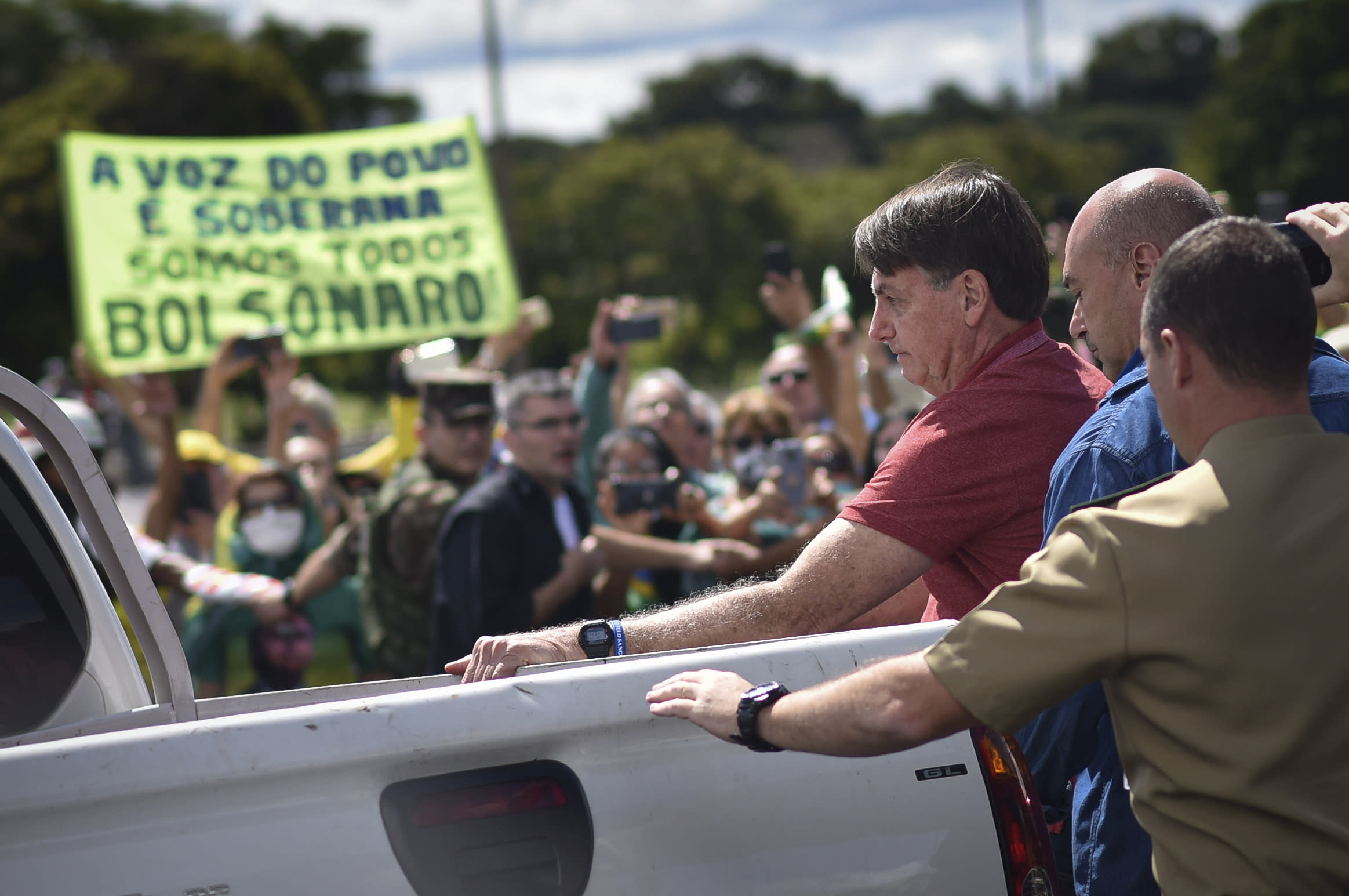 Brazil's President Jair Bolsonaro appears at a protest asking for military intervention in front the army's headquarters during the new coronavirus pandemic, in Brasilia, Brazil, Sunday, April 19, 2020. Bolsonaro came out in support of a small protest Sunday that defended military intervention, infringing his own ministry's recommendations to maintain social distancing and prompting fierce critics. (AP Photo/Andre Borges)