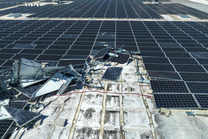 Broken down photovoltaic solar panels destroyed by hurricane Ian winds mounted on industrial building roof for producing green ecological electricity. Consequences of natural disaster.