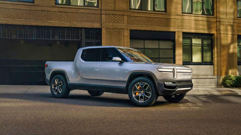 A silver Rivian R1T EV pickup truck parked out front of a brick building late in the day with shadows and low evening sun.