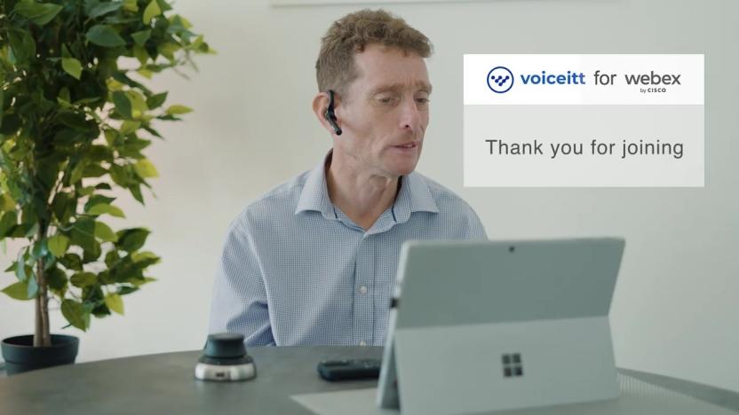 A man sits on a web call with a transcription of his speech beside him. 