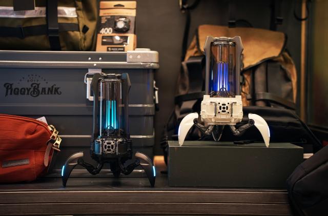 Two Bluetooth speakers that look like bug-like droids from a sci-fi film. They sit on a dark-colored desk with various objects.