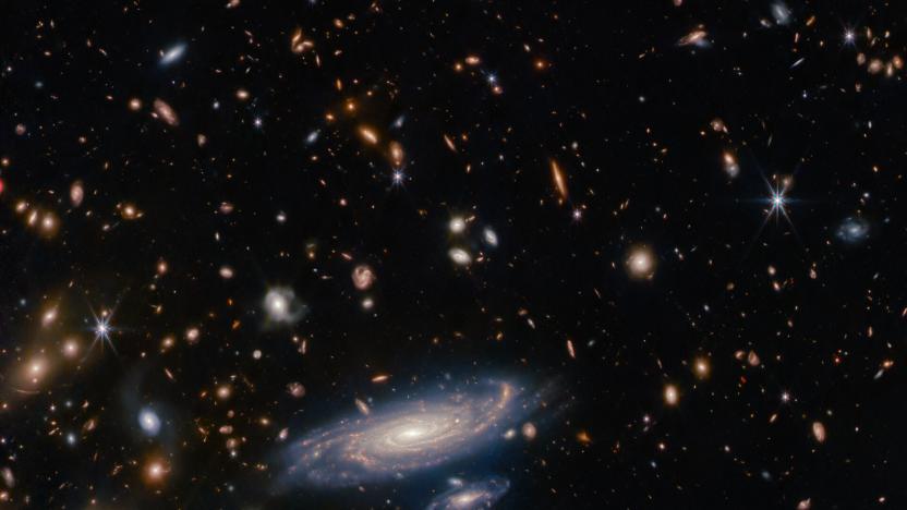 Image that was taken with the James Webb Space Telescope showing a spiral galaxy at the bottom center, surrounded by more distant galaxies (appearing as blobs) and individual stars.