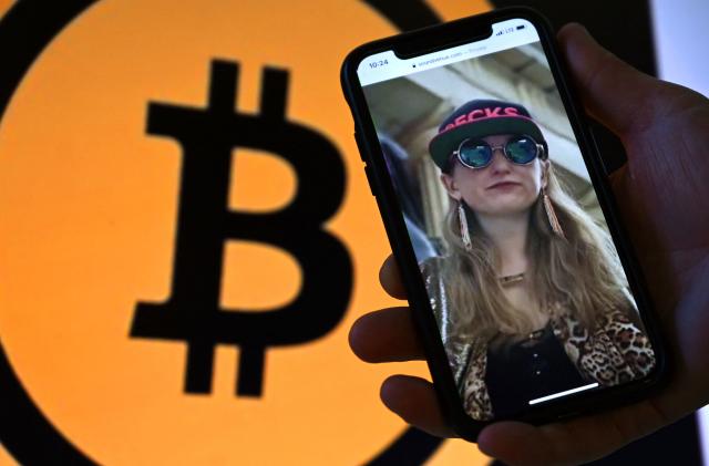 This illustration photo shows Heather Morgan, also known as "Razzlekhan," on a phone in front of the Bitcoin logo displayed on a screen, in Washington, DC, February 9, 2022. - A couple accused of seeking to launder the bitcoin were arrested in New York, the department said. Ilya Lichtenstein, 34, and his wife Heather Morgan, 31, were set to appear in federal court over the charges later in the day. (Photo by Olivier DOULIERY / AFP) (Photo by OLIVIER DOULIERY/AFP via Getty Images)