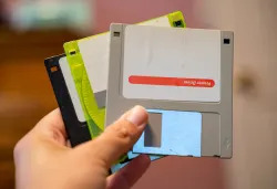 Hand holds out Three outdated 3.5 inch floppy disks, from the 1990s