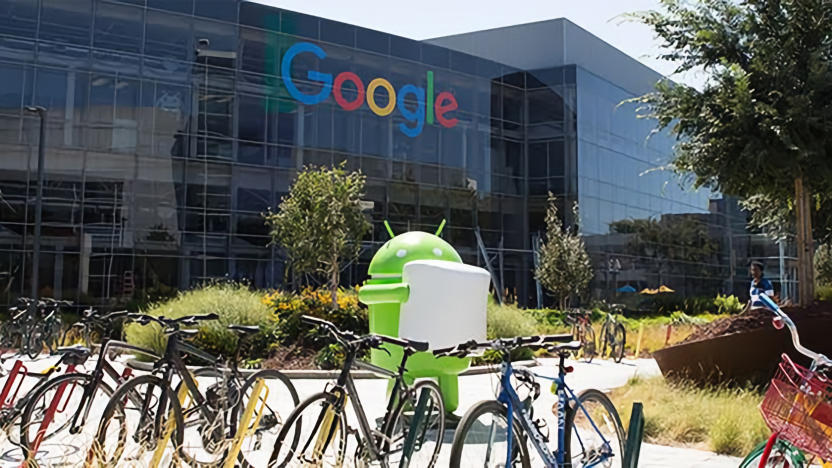 Photo of the Googleplex (outdoor view) with Google logo in the background. An Android Marshmallow statue stands behind a full bicycle rack.