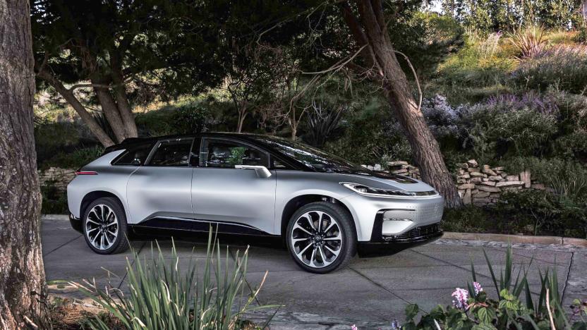 A photo of a silver Faraday Future FF91 2.0 Futurist Alliance electric vehicle parked on the road against a background of trees and grass.