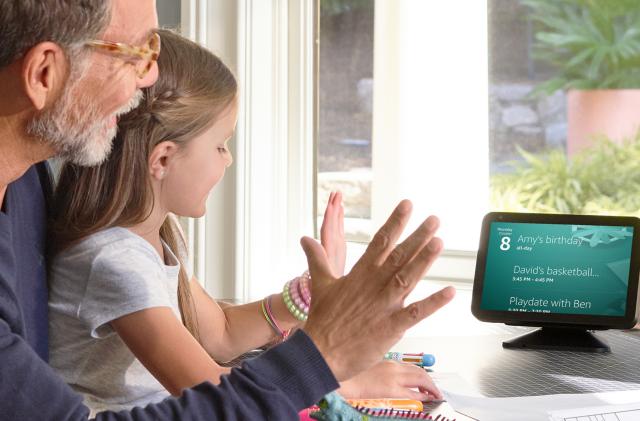 A father and daughter sitting in front of an Echo Show, holding their palms in the air to dismiss a timer.