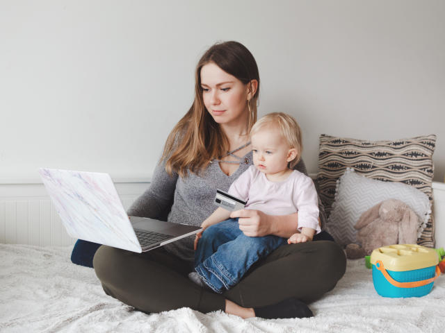 Young Caucasian mother with baby shopping online from home. Stay at home single mom with kid toddler daughter buying ordering products food on Internet and paying with credit card.