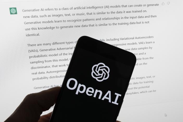 FILE - The OpenAI logo is seen on a mobile phone in front of a computer screen displaying output from ChatGPT, March 21, 2023, in Boston. OpenAI plans to halt the use of one of its ChatGPT voices after some drew similarities to actor Scarlett Johansson, who famously portrayed a fictional AI assistant in the (perhaps no longer so futuristic) film “Her.” (AP Photo/Michael Dwyer, File)