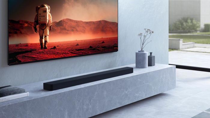 A black soundbar on a shelf just below a TV with an astronaut in space gear walking on a distant plant displayed on screen. 