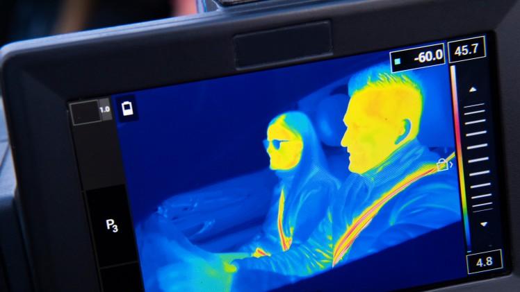 thermal camera view of two people pretending to drive a car while their seatbelts burn stripes in thier torsos