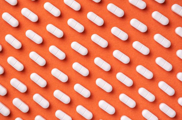 Orange and red medicine background with white pills and tablet, macro. Drug production backdrop. Medical pattern from vitamin capsule, closeup.