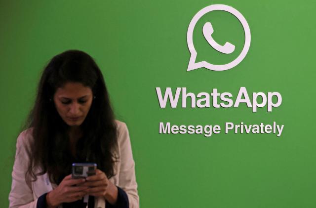 A woman uses her phone next to a logo of the WhatsApp application during Global Fintech Fest in Mumbai, India September 20, 2022. 