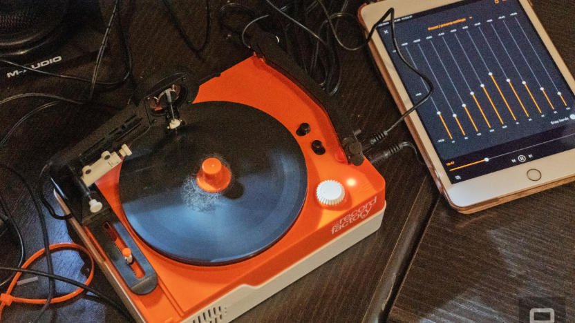 The Teenage Engineering Record Factory vinyl cutter in orange and white seen on a table cluttered with cables, audio gear and speakers.