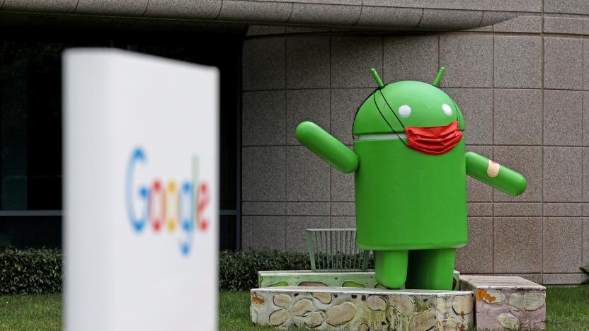 An image from outside of the Google campus building in Mountain View, CA. showing an out of focus Google sign in the foreground and an Android statue with an ad-hoc face mask behind it.

