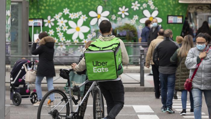 Madrid, Spain - Nov 25, 2020: A worker, a food delivery delivery man for the Uber Eats company, walks with his bicycle and crosses Narvaez street