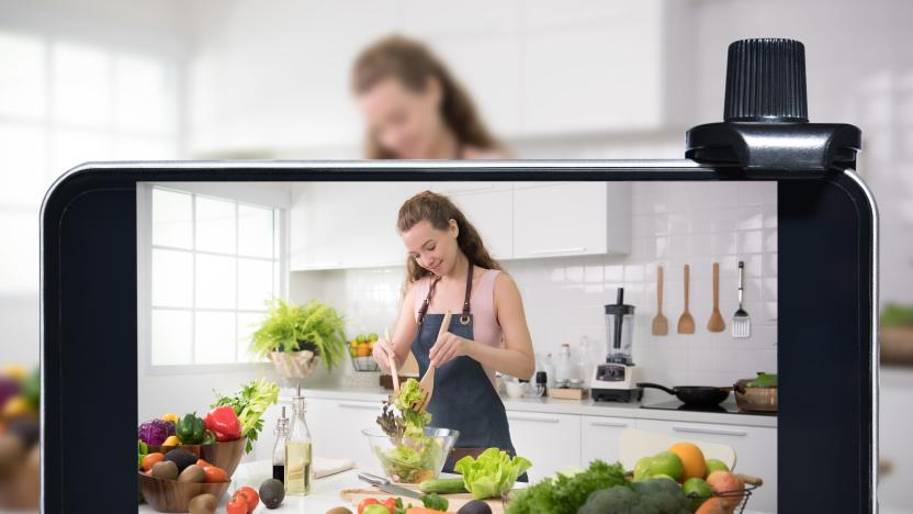 A young female blogger and vlogger and online influencer live streaming a cooking show on social media using a smartphone