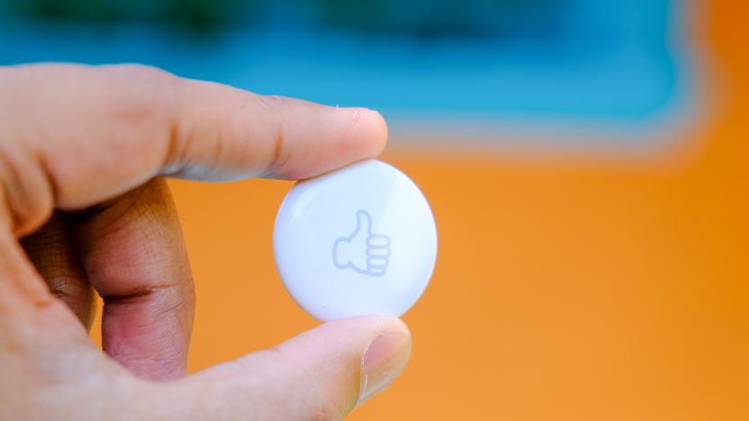 A hand holds a white circular object with a gray thumbs up on it. 