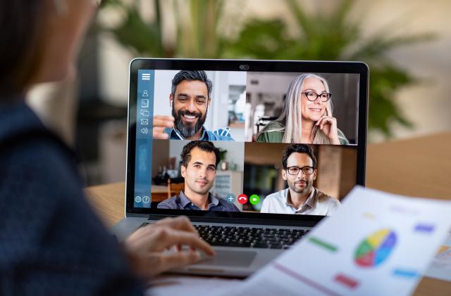 Back view of business woman talking to her colleagues about business plan in video conference. Multiethnic business team using laptop for a online meeting in video call. Group of businessmen and businesswomen smart working from home.