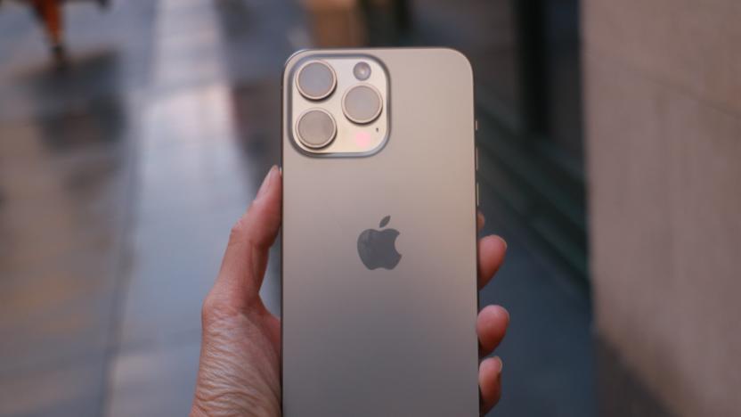 The iPhone 15 Pro Max held in mid-air with a sidewalk in the background.