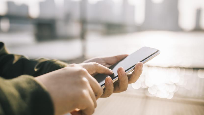 Close up of man's hand using smartphone on the go in the city against sunlight.