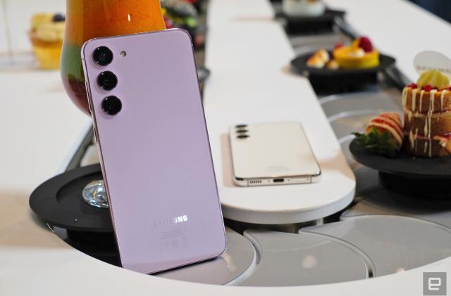 A Samsung Galaxy S23+ smartphone is propped up in the middle of a conveyor belt with food.