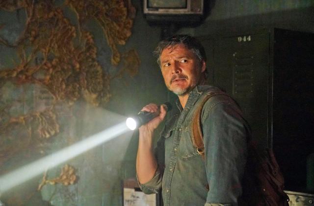 Pedro Pascal as Joel in HBO's 'The Last of Us' stands in a dimly lit room while holding a flashlight to look around.