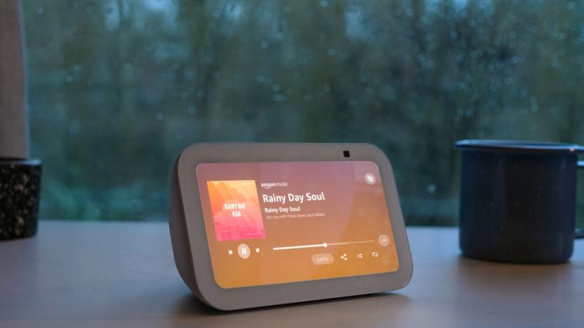 Amazon's Echo Show 5 smart display rests on a tablet in front of a rainy window.