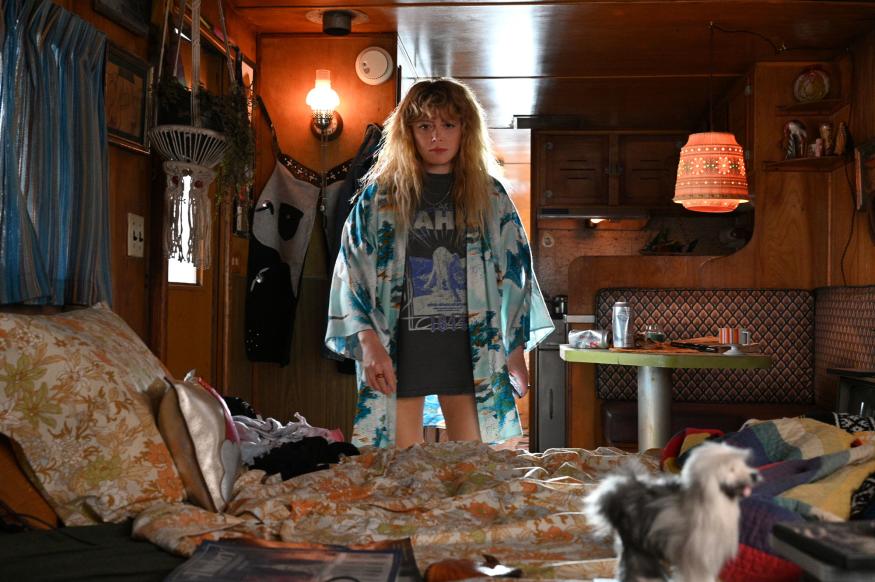 Image of actress Natasha Lyonne, star of the new series 'Poker Face', staring toward the camera and the middle distance. She is in a wood-pannelled room with distinctly retrograde styling, evoking memories of terrible holidays from the '70s. 
