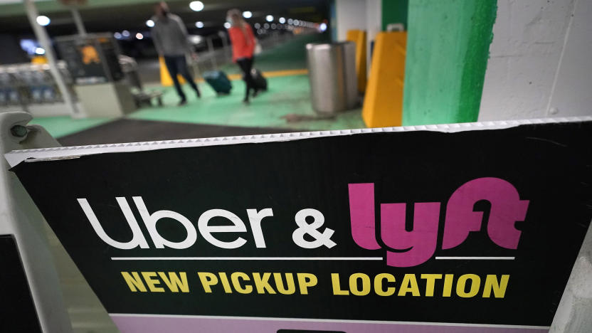Passers-by pull luggage as they walk near a sign advising travelers of an Uber and Lyft pickup location at Logan International Airport, in Boston, Tuesday, Feb. 9, 2021. (AP Photo/Steven Senne)