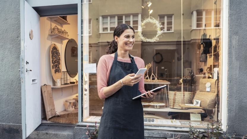 Smiling female entrepreneur with smart phone and digital tablet outside store